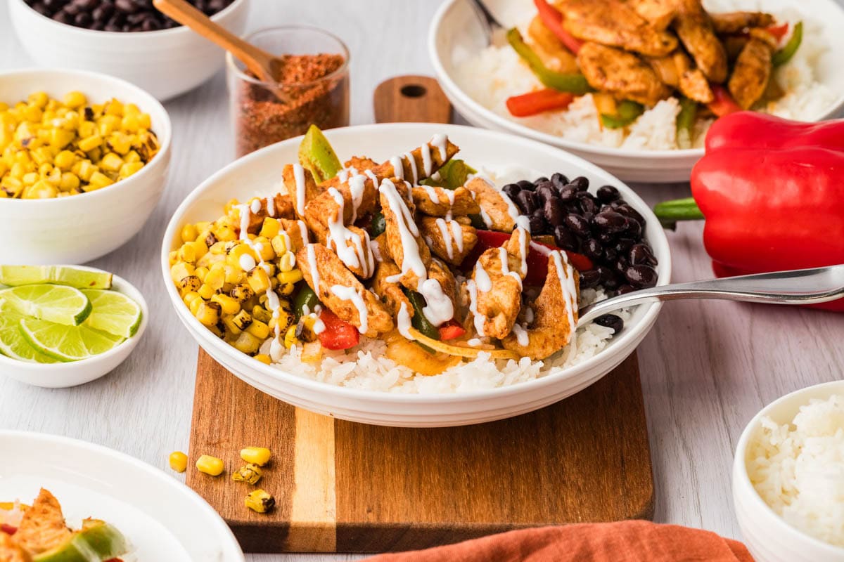 Two chicken fajita bowls, one served with black beans and corn on a wooden board.