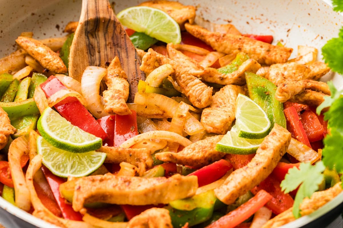 Close up of chicken and fajita veggies cooking in a skillet.