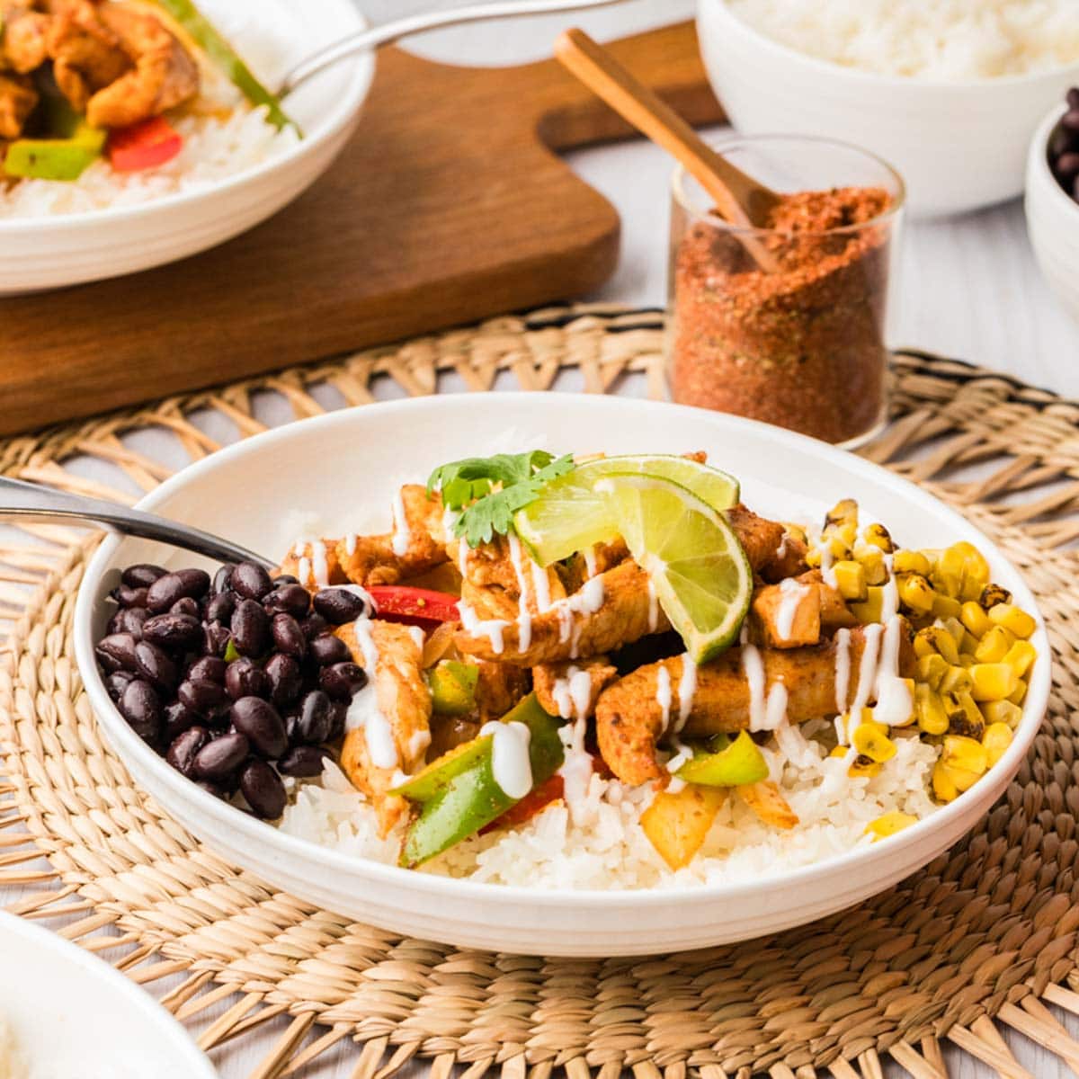Side view of chicken fajita bowls with rice, black beans, corn and sour cream on top.