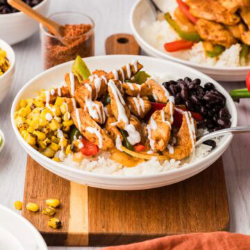 Chicken fajita bowl served with rice, corn and black beans on a wooden board.