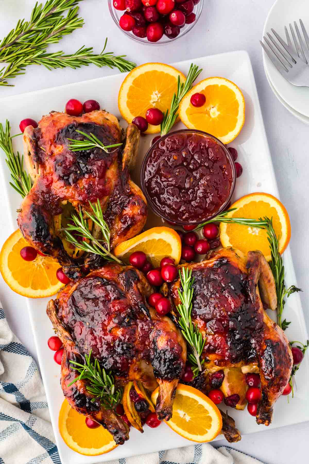 Three Cornish hens served on a platter with orange slices, cranberries and rosemary.