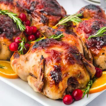 Cranberry orange glazed Cornish hens on a serving platter garnished with rosemary.