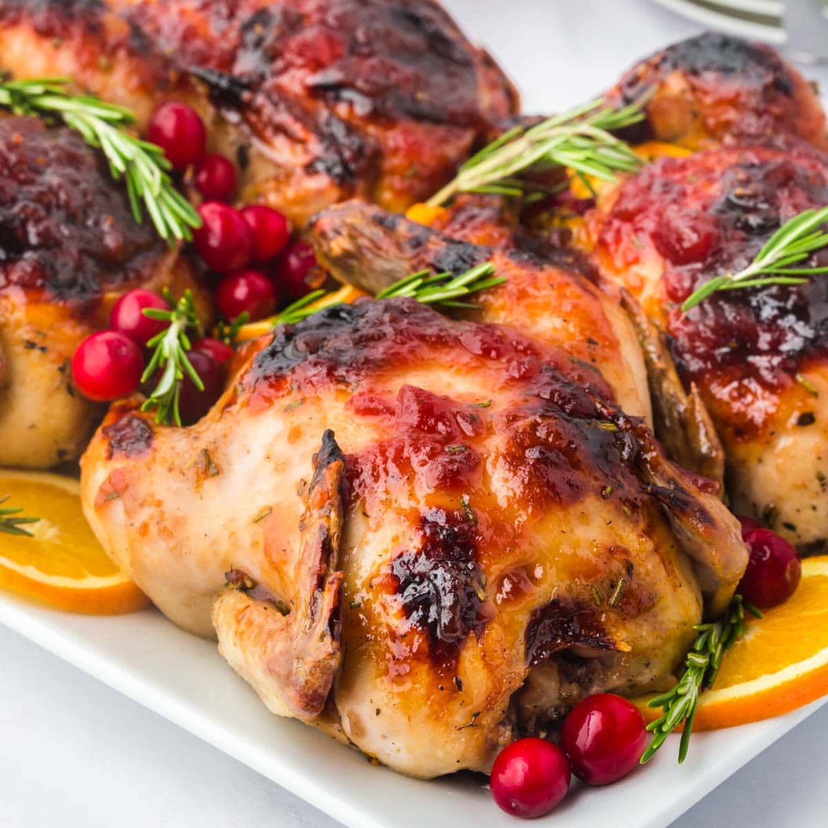 Cranberry orange glazed Cornish hens on a serving platter garnished with rosemary.