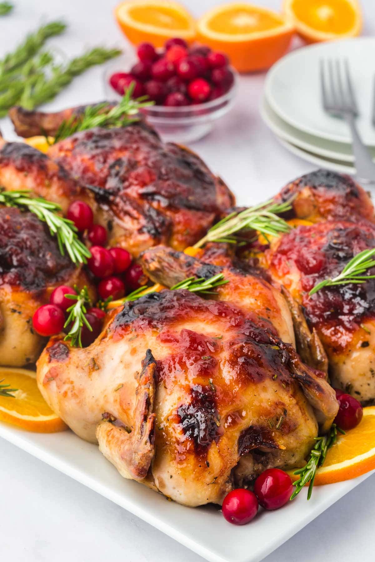 Cranberry orange glazed Cornish hens served on a plate with cranberry and rosemary garnish.