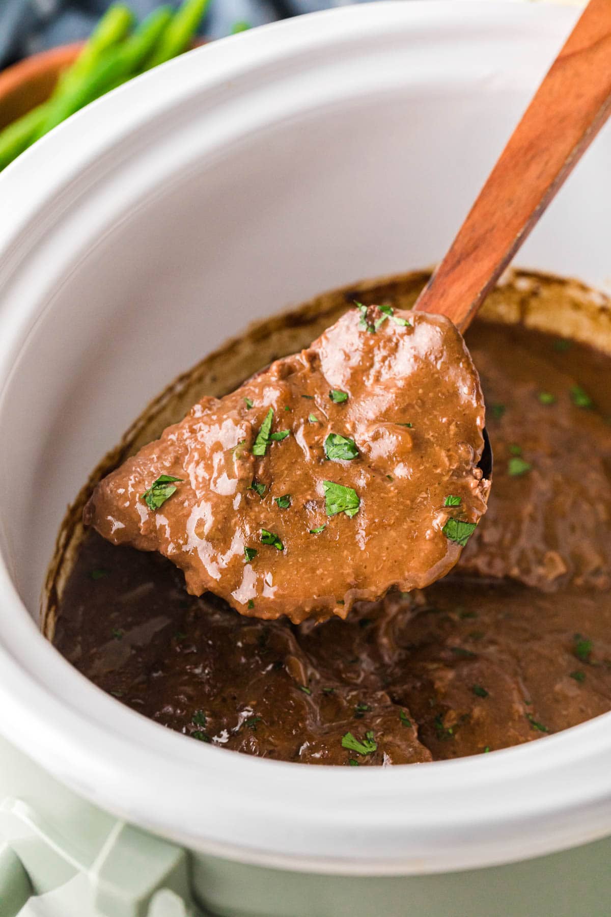 A wooden spoon, removing one country steak out of a slow cooker.
