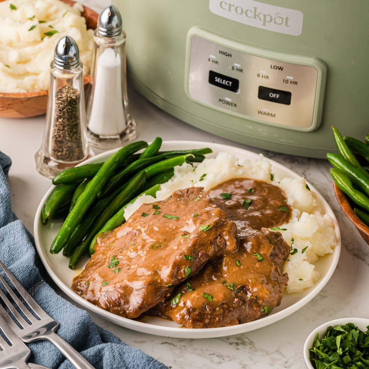 Crockpot cubed steak and gravy on a whit plate served with mashed potatoes and gravy.