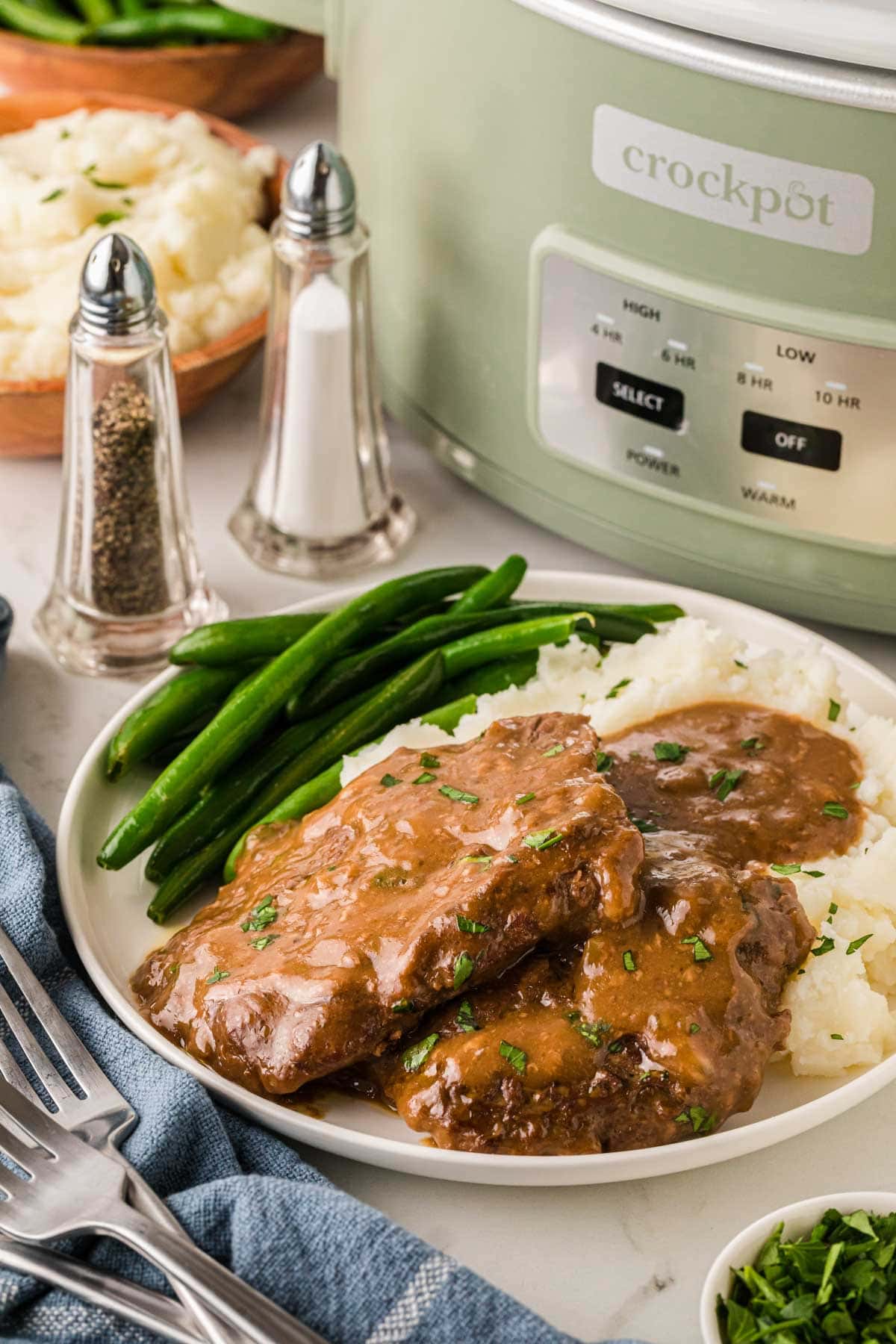 Slow Cooker cubed steak and gravy on a whit plate served with mashed potatoes and gravy.