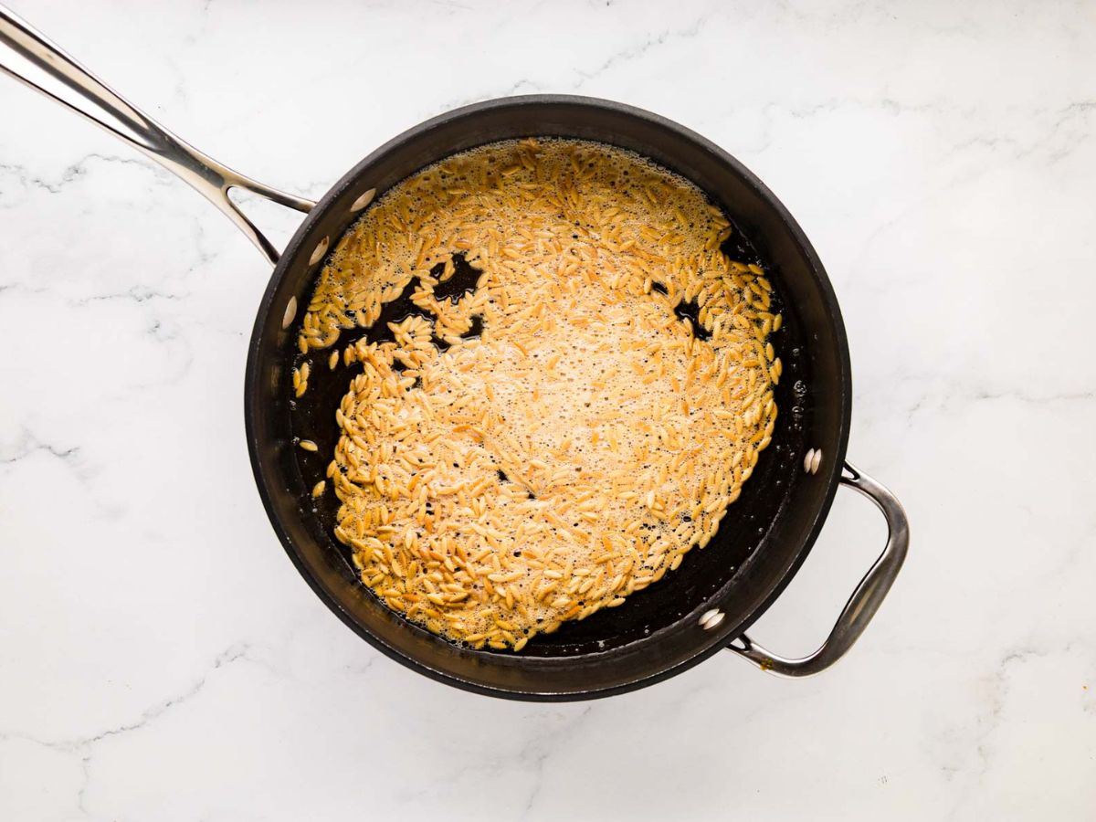 Toasted orzo in a skillet.