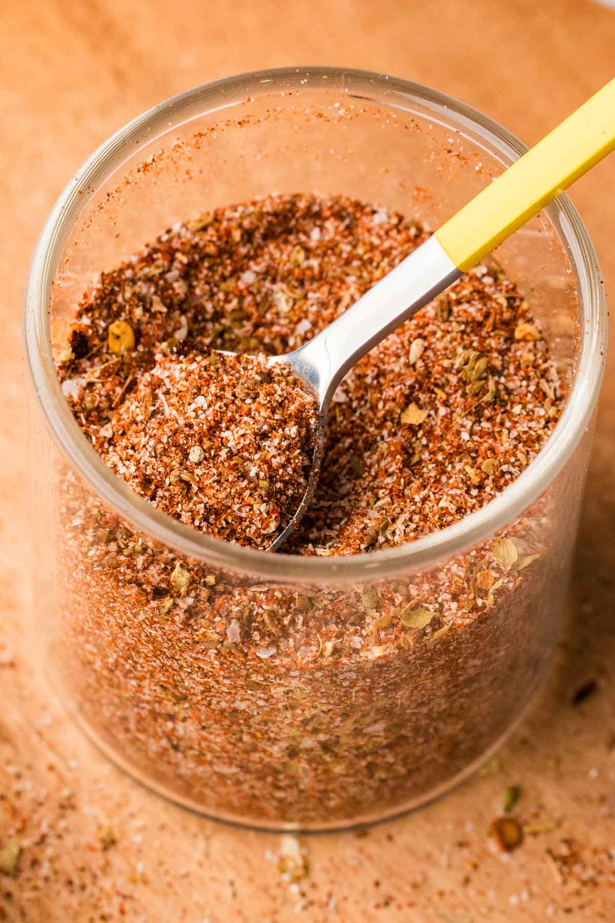 Homemade fajita seasoning in a glass container with a small spoon inside.