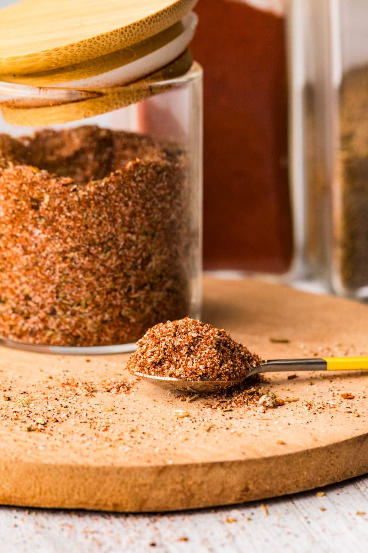 Spoon piled high with fajita seasoning with the glass container behind it.