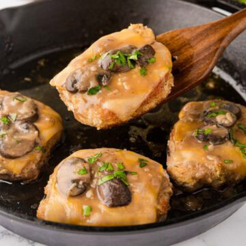 Fontina pork chop with marsala mushroom sauce removed from skillet with a wooden spatula.