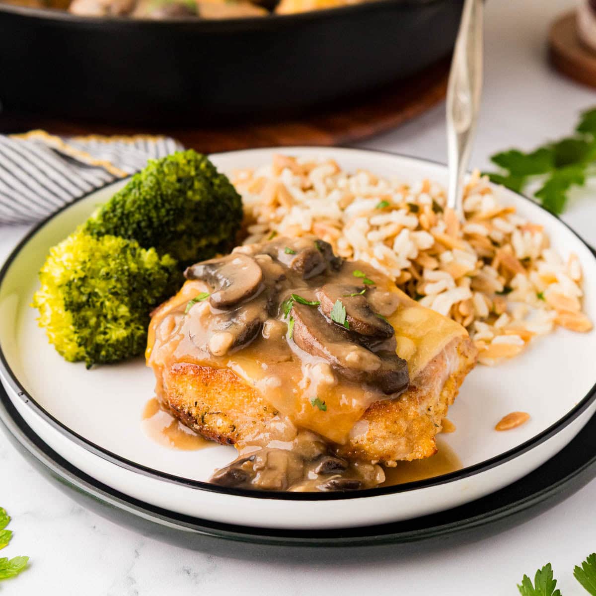 Fontina pork chop with marsala mushroom sauce on a plate with rice and broccoli.