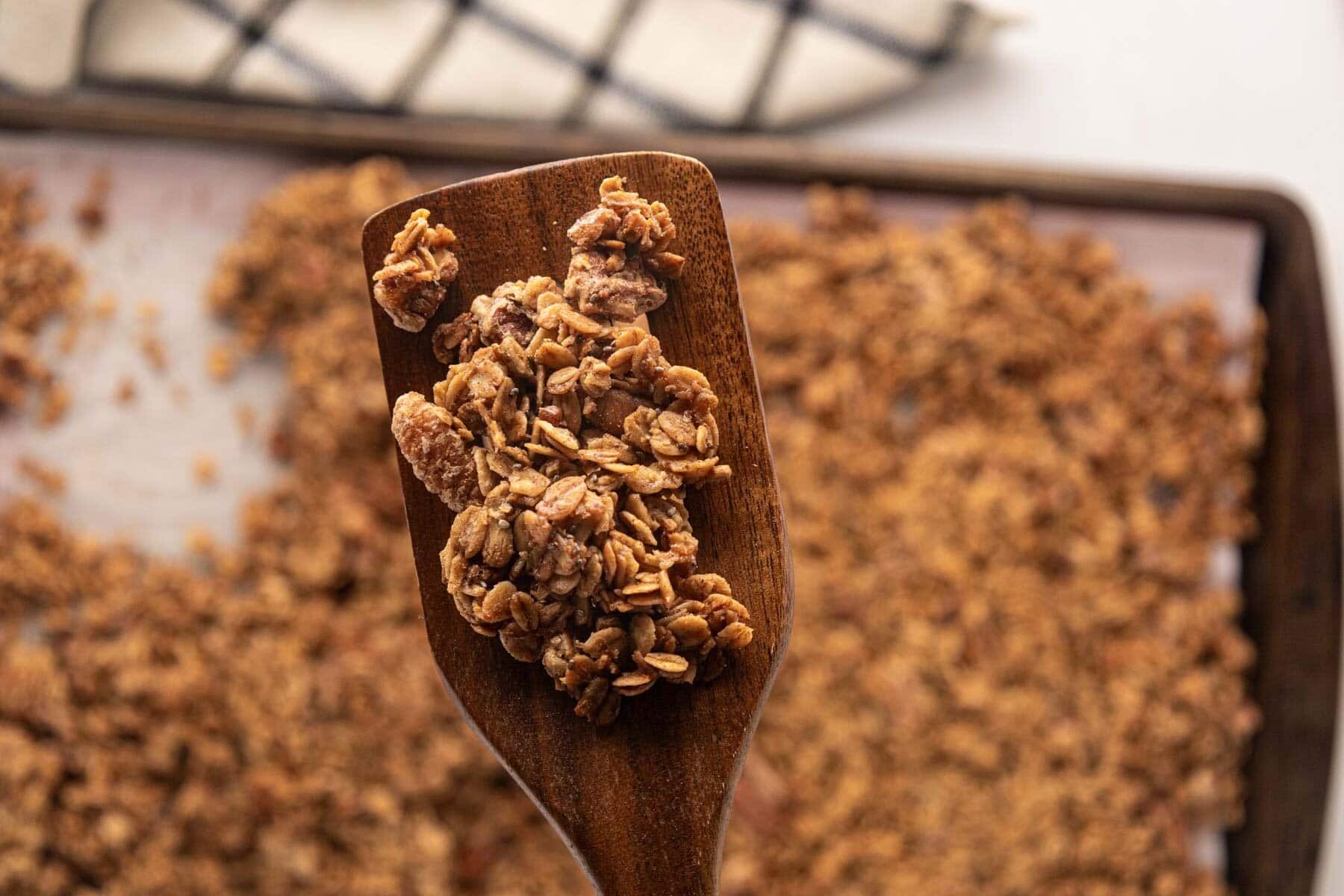 A wooden spatula, removing a cluster of granola from the baking sheet.