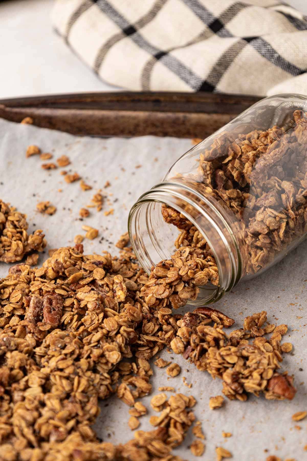 Granola made with pecans and maple syrup on a baking sheet being put into a mason jar.