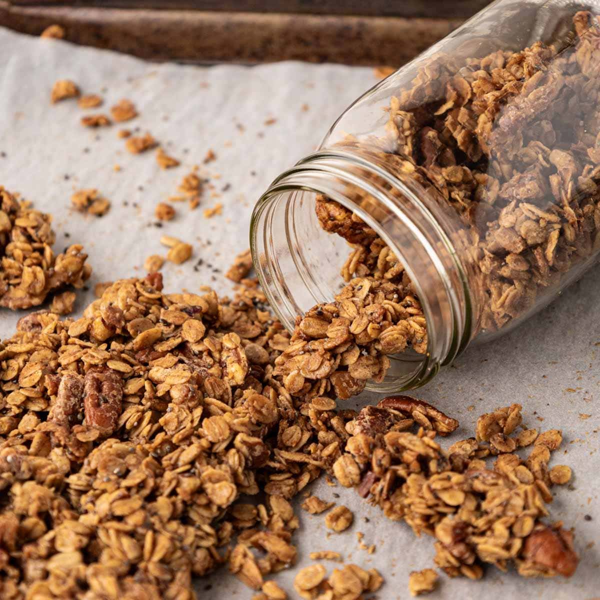 Granola made with pecans and maple syrup on a baking sheet being put into a mason jar.