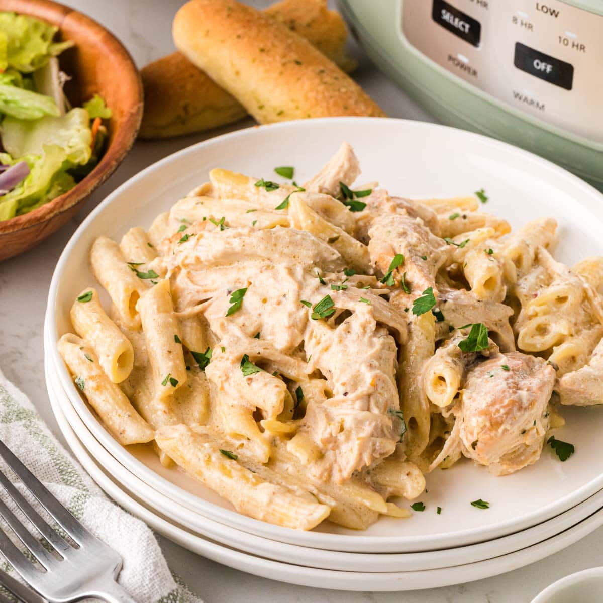 Olive garden chicken pasta on a plate with a crockpot in the background.