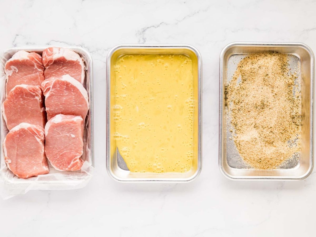 Three shallow dishes, one with season pork chop chops, one with egg and one with seasoned breadcrumbs.