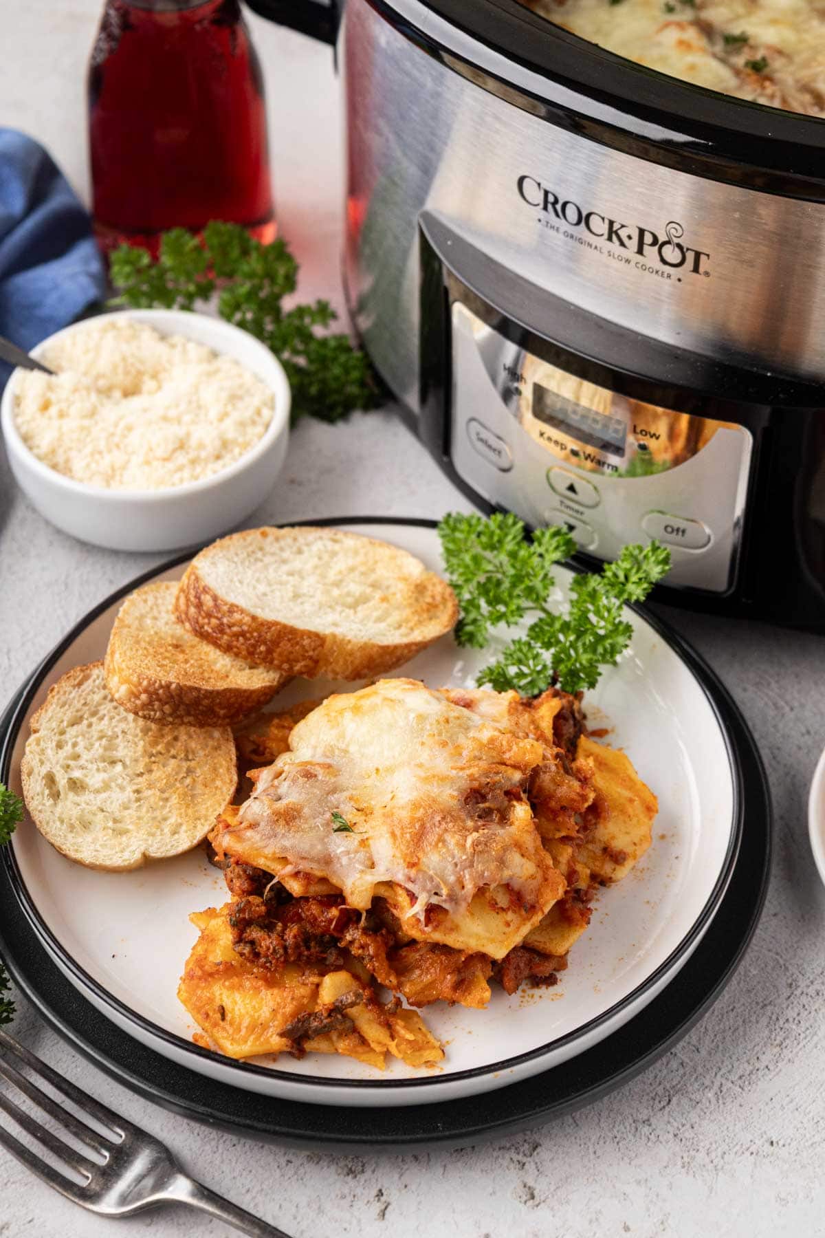 A serving ravioli lasagna made in the slow cooker on a white plate with garlic bread.