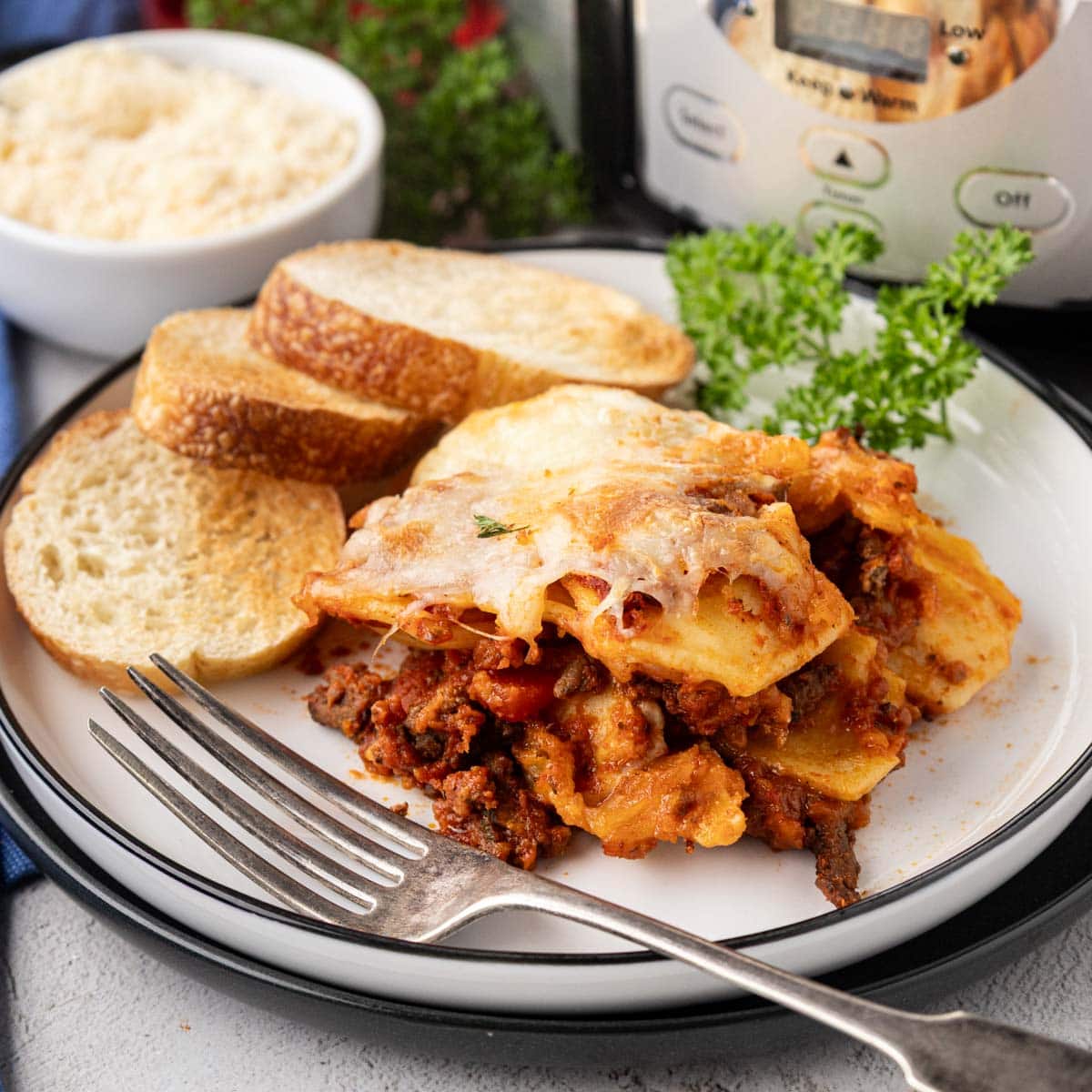 A serving ravioli lasagna made in the slow cooker on a white plate with garlic bread.