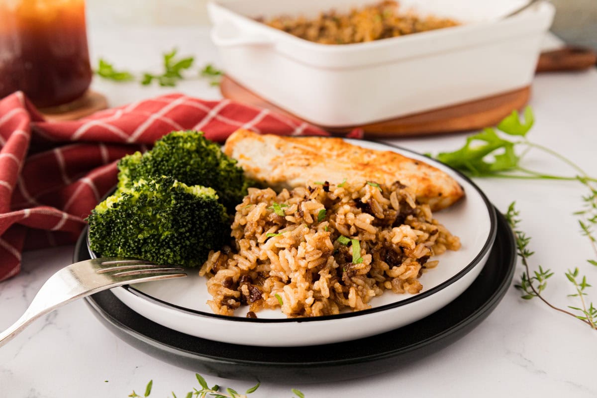 A white plate with French onion rice served with broccoli and chicken.