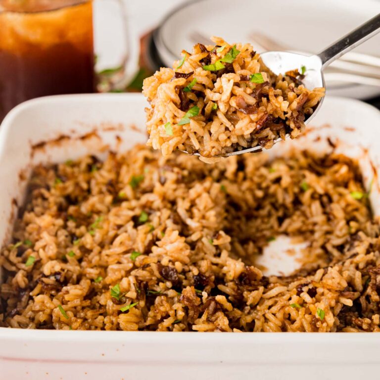 A serving spoon removing a scoop of stick of butter french onion rice from a casserole dish.