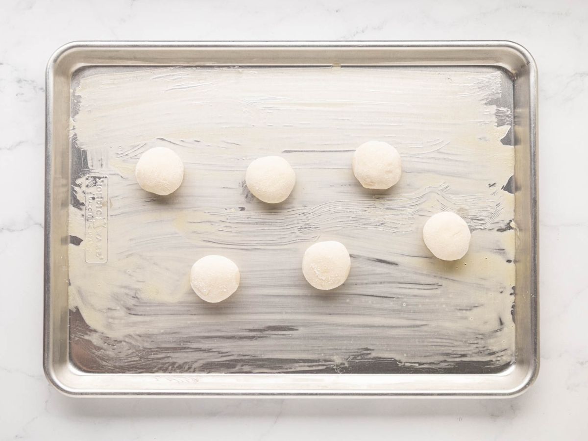 Frozen bread dough rolls thawing on a baking sheet.