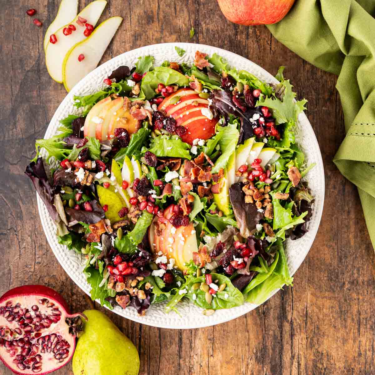 A white bowl filled with mixed greens, apples, pears, feta and fall, seasonal nuts, and fruits.