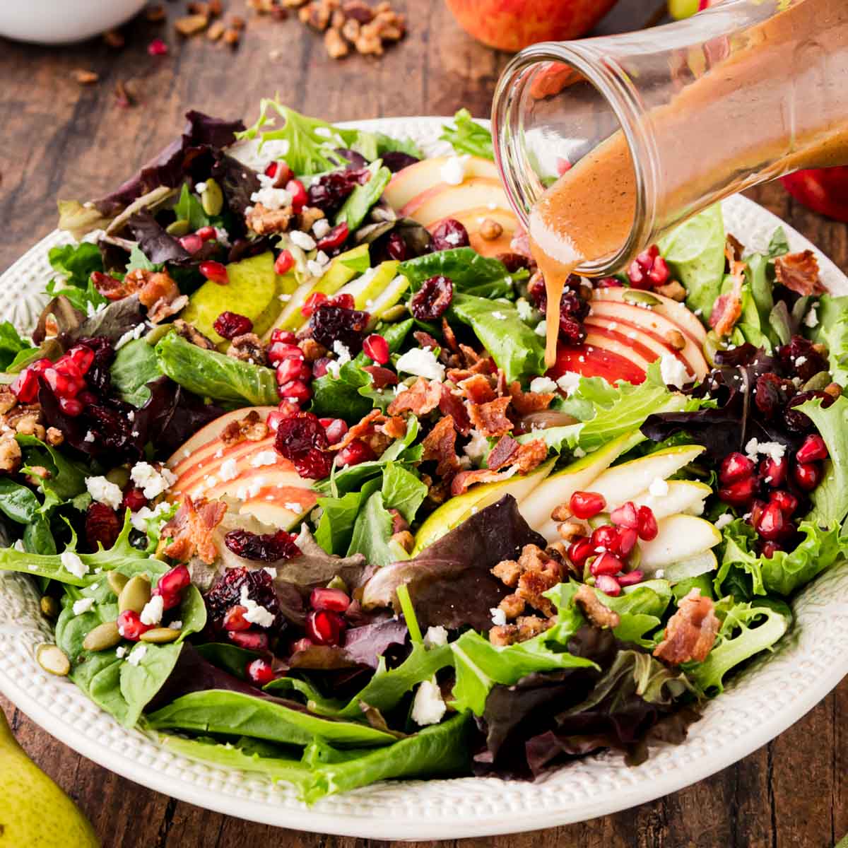 A bowl filled with a fall harvest salad and a apple vinaigrette being poured over top.