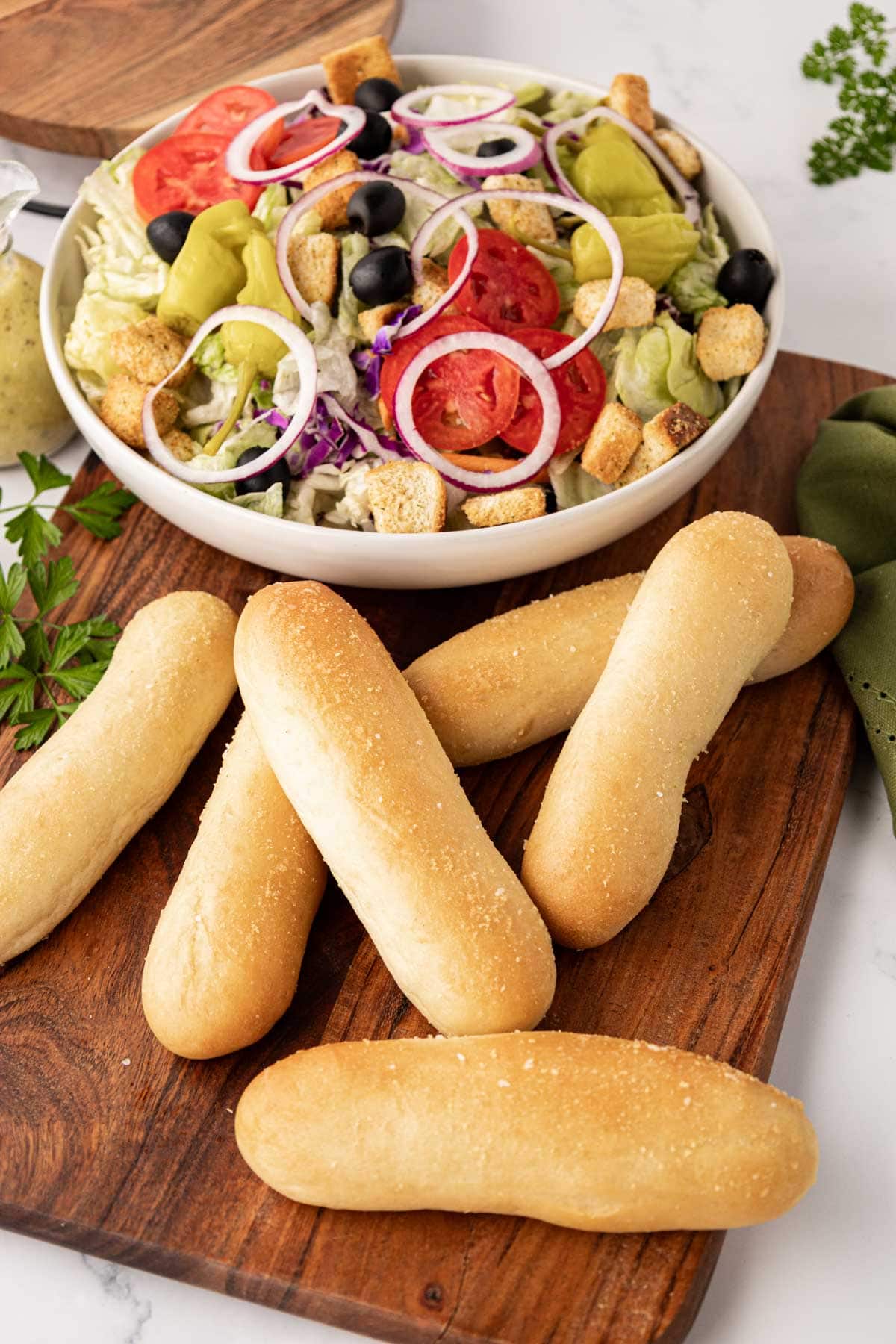 Golden baked breadsticks on a wooden board with a side salad in the background.