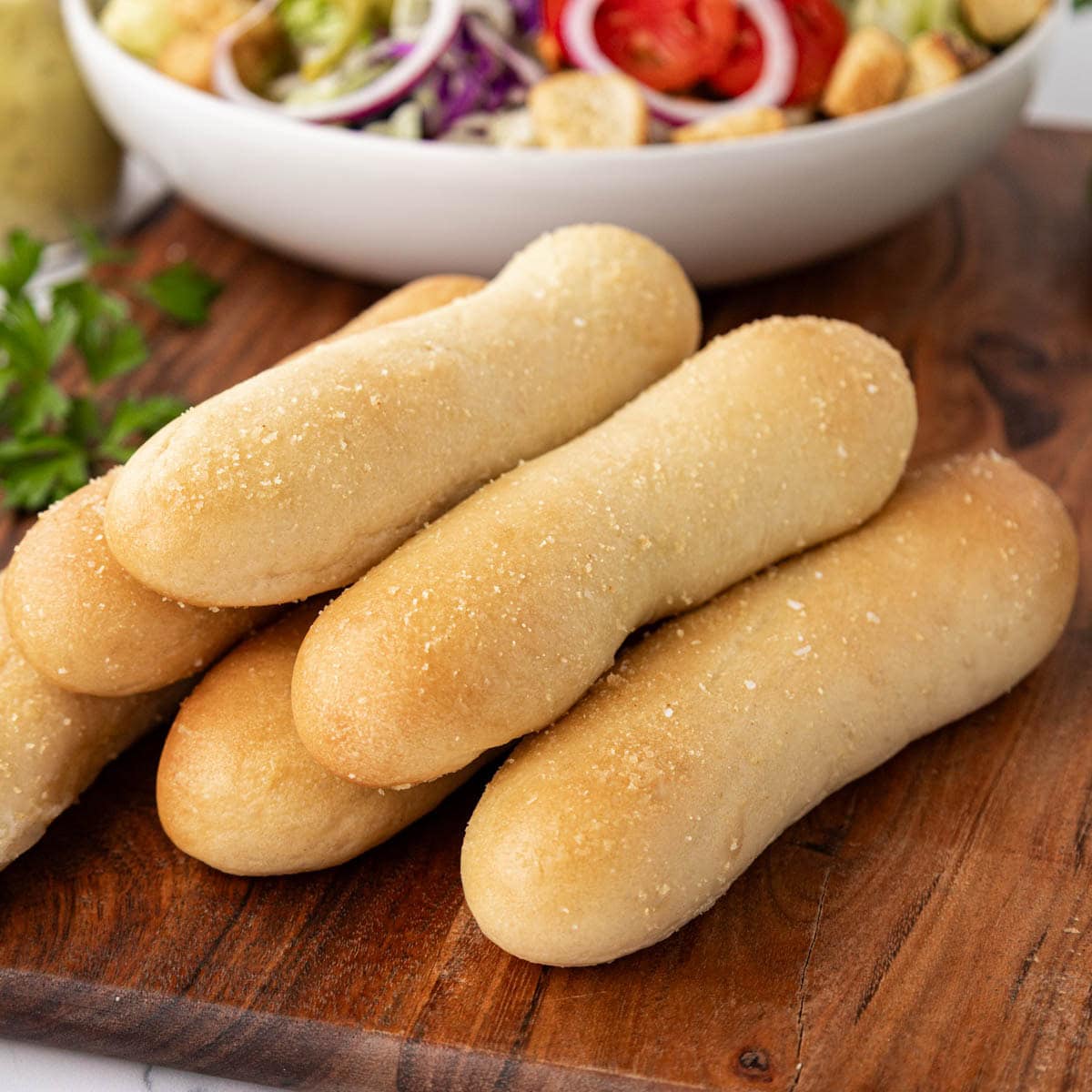 Golden baked breadsticks on a wooden board with a side salad in the background.