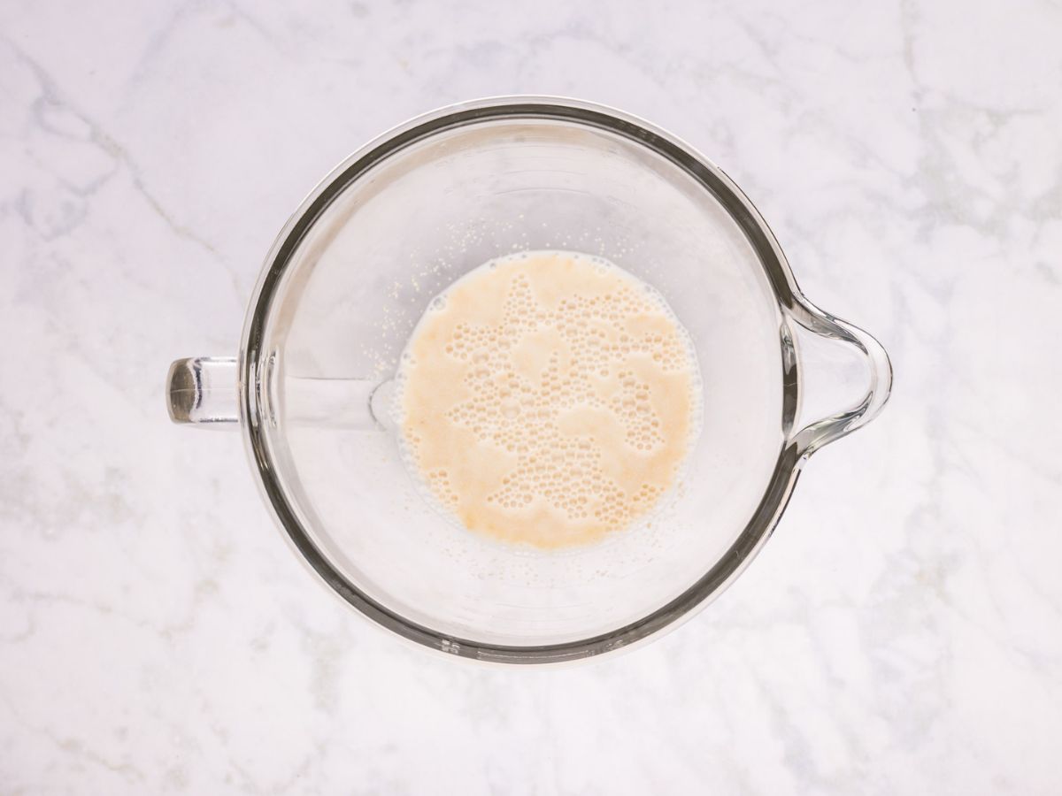 Milk, sugar and yeast in the mixing bowl of a stand mixer.