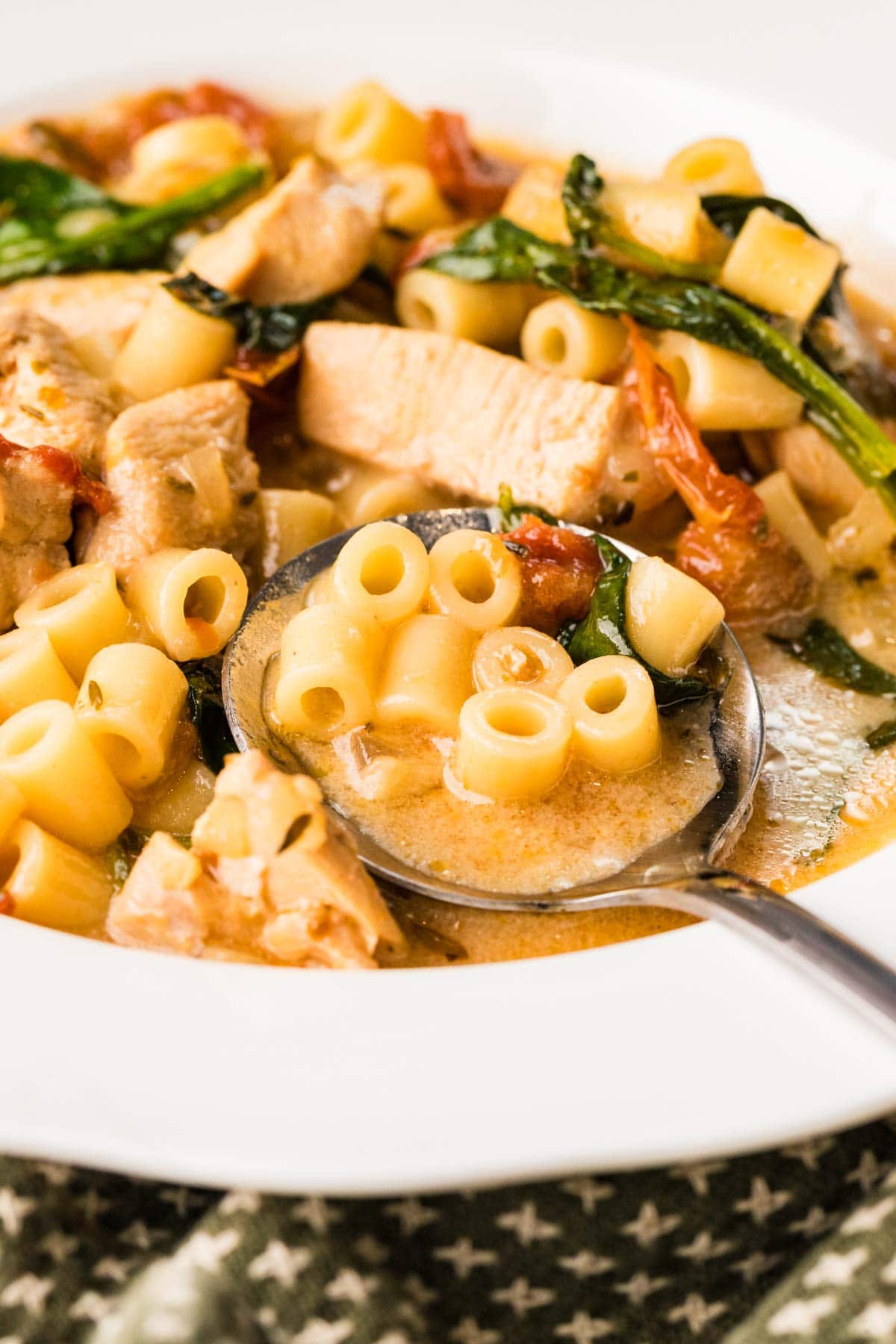 Close up of a bowl of marry me chicken soup with a spoon full of soup on the edge of the bowl.