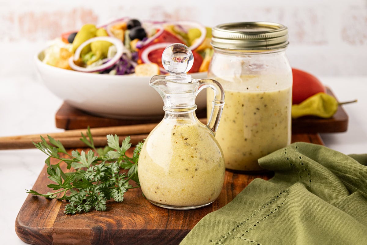 Homemade Copycat Olive Garden Salad dressing in a bottle and mason jar with a salad in the background.