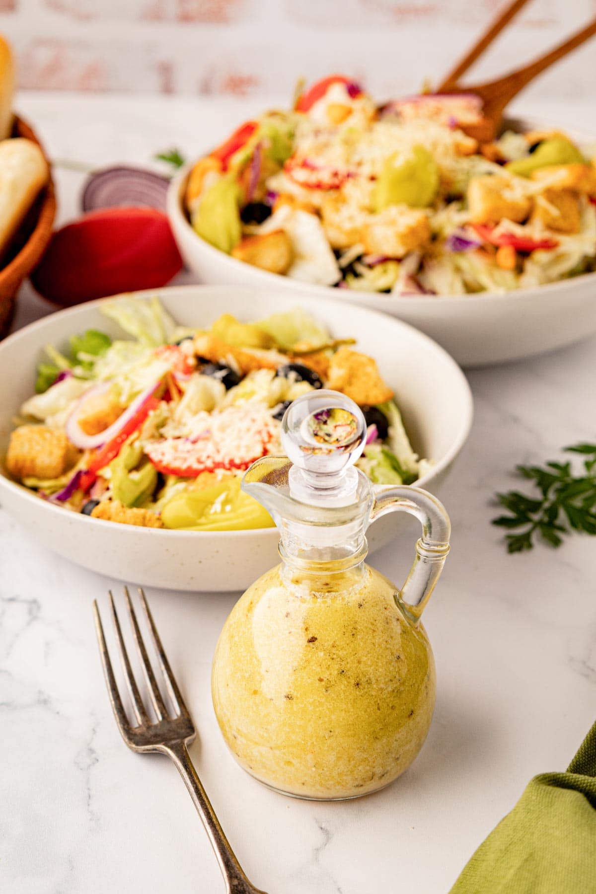 A salad dressing bottle filled with Olive Garden copycat dressing with a bowl and plated salad in the background.