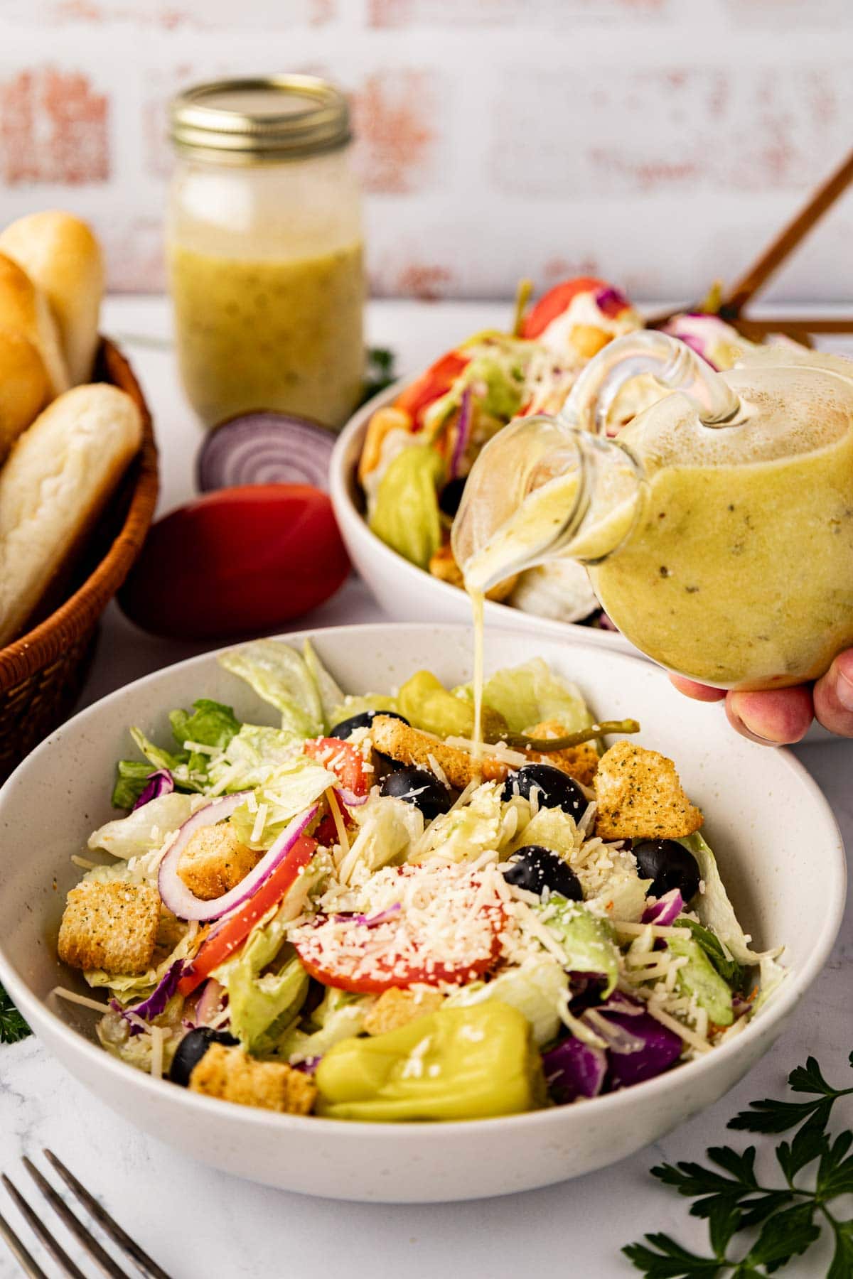 Pouring salad dressing on top of copycat Olive Garden salad in a white bowl.