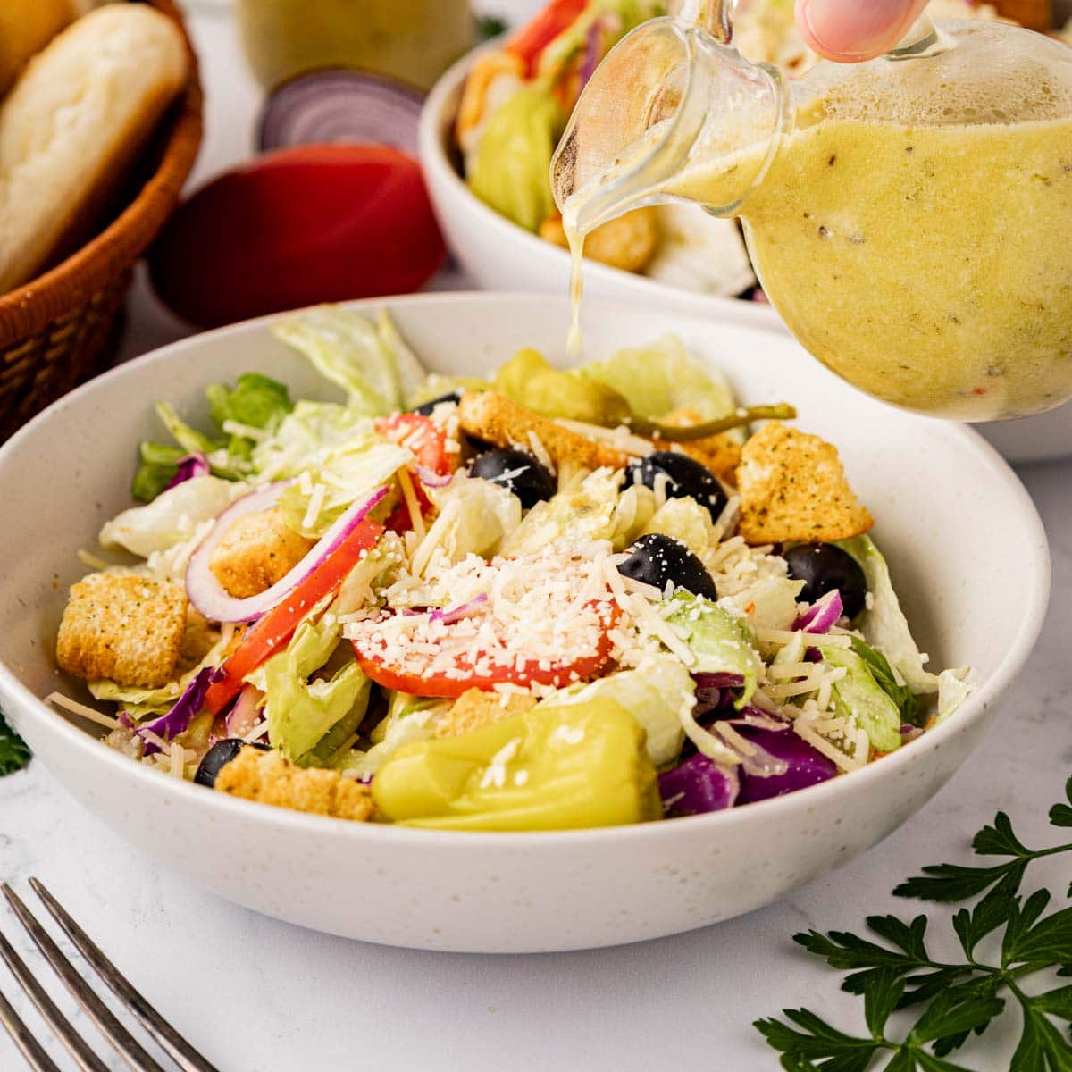 Pouring salad dressing on top of copycat Olive Garden salad in a white bowl.