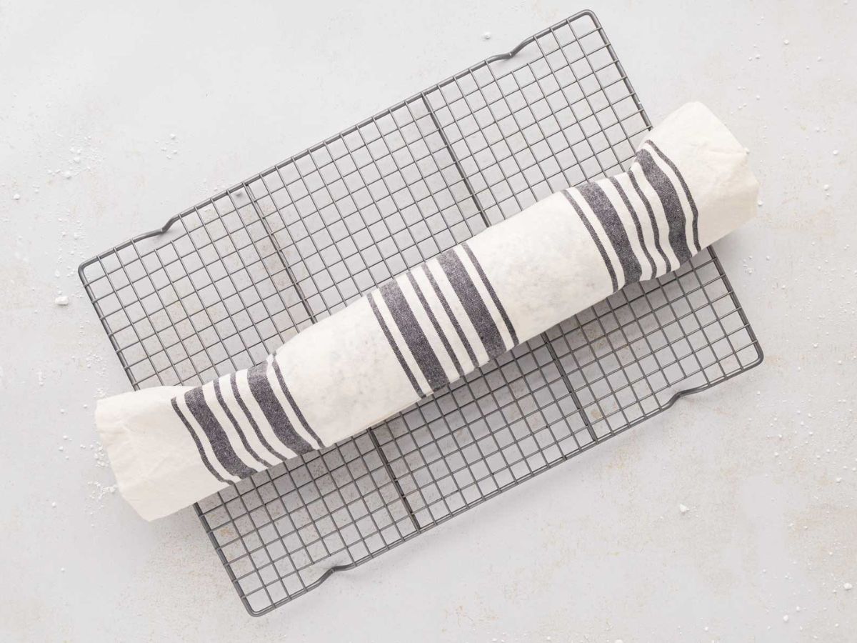 Pumpkin roll cake all rolled up in a tea towel cooling on a wire rack.