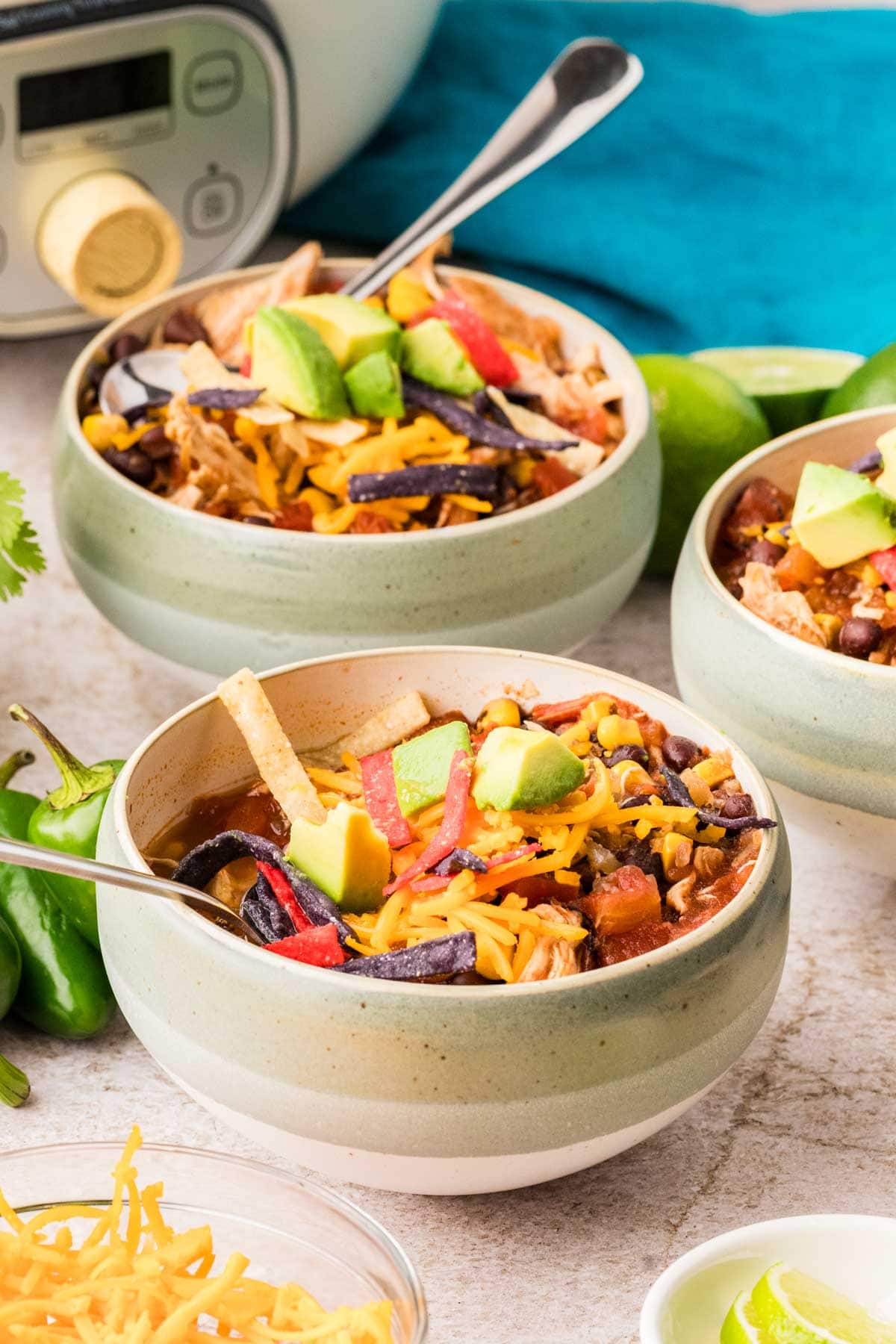 Two bowls of chicken tortilla soup both topped with cheese, tortilla strips and avocado.