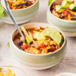 Bowl of slow cooker chicken tortilla soup garnished with avocado and lime wedges.