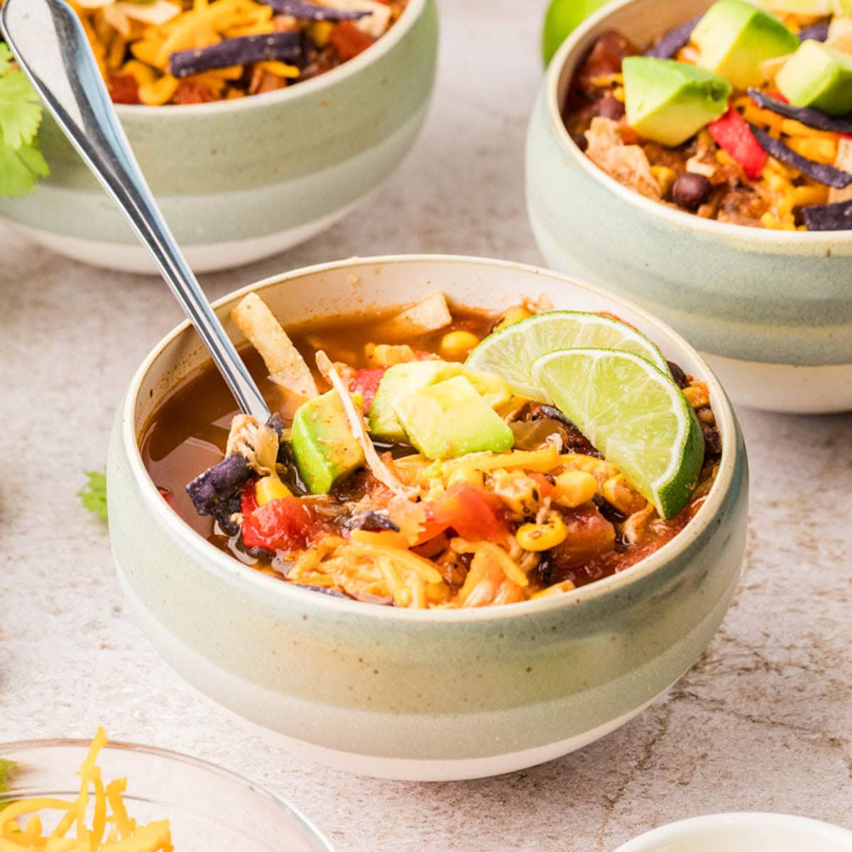 Bowl of slow cooker chicken tortilla soup garnished with avocado and lime wedges.