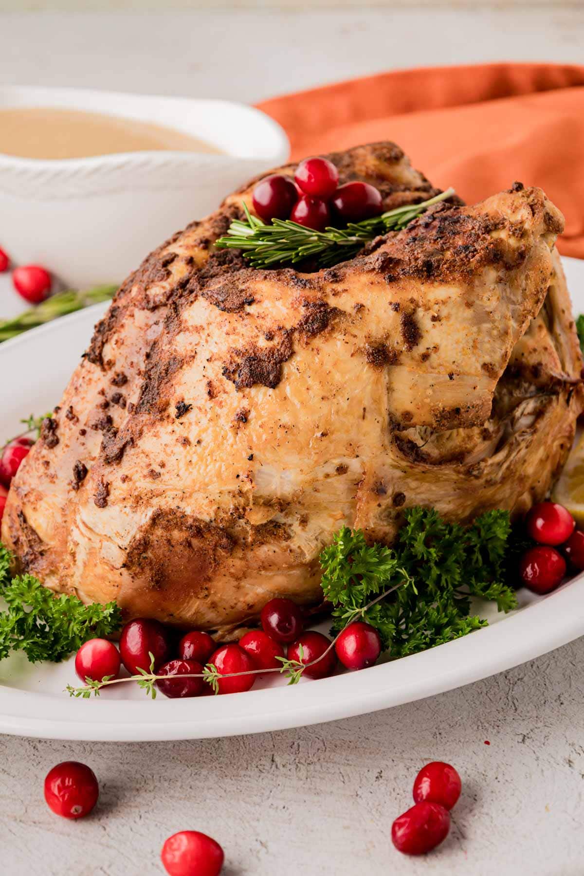 A whole turkey breast that was cooked in the crockpot on a platter, garnished with parsley, cranberries, and rosemary.