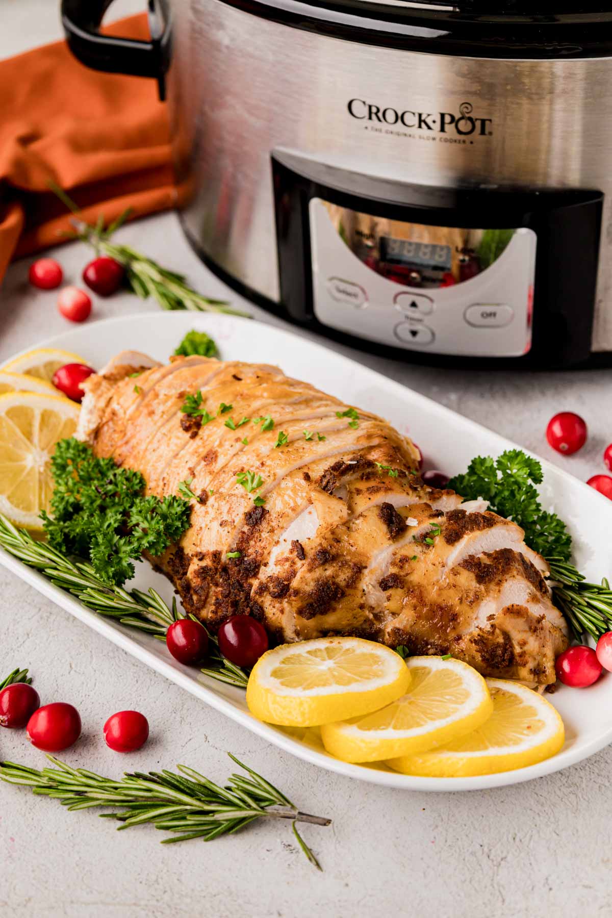 A sliced turkey breast made in the slow cooker with a crockpot in the background.