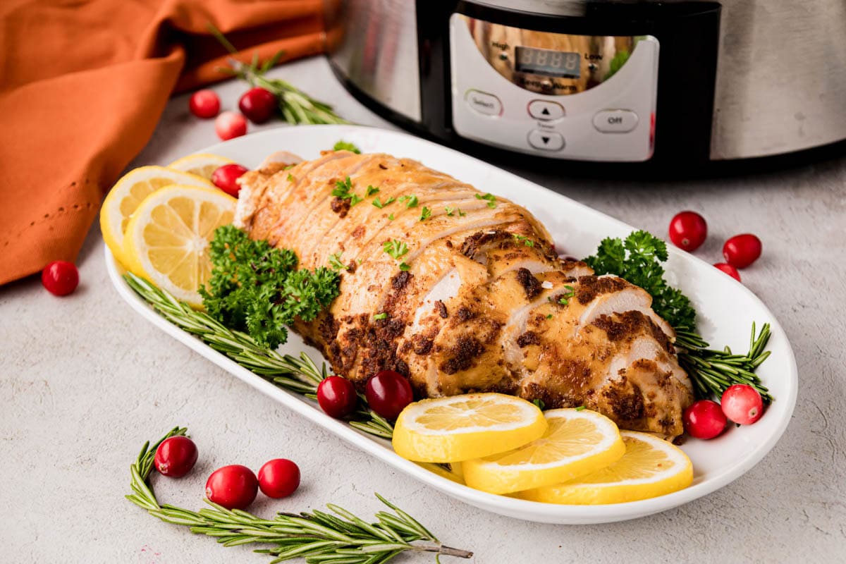 A sliced turkey breast made in the slow cooker with a crockpot in the background.