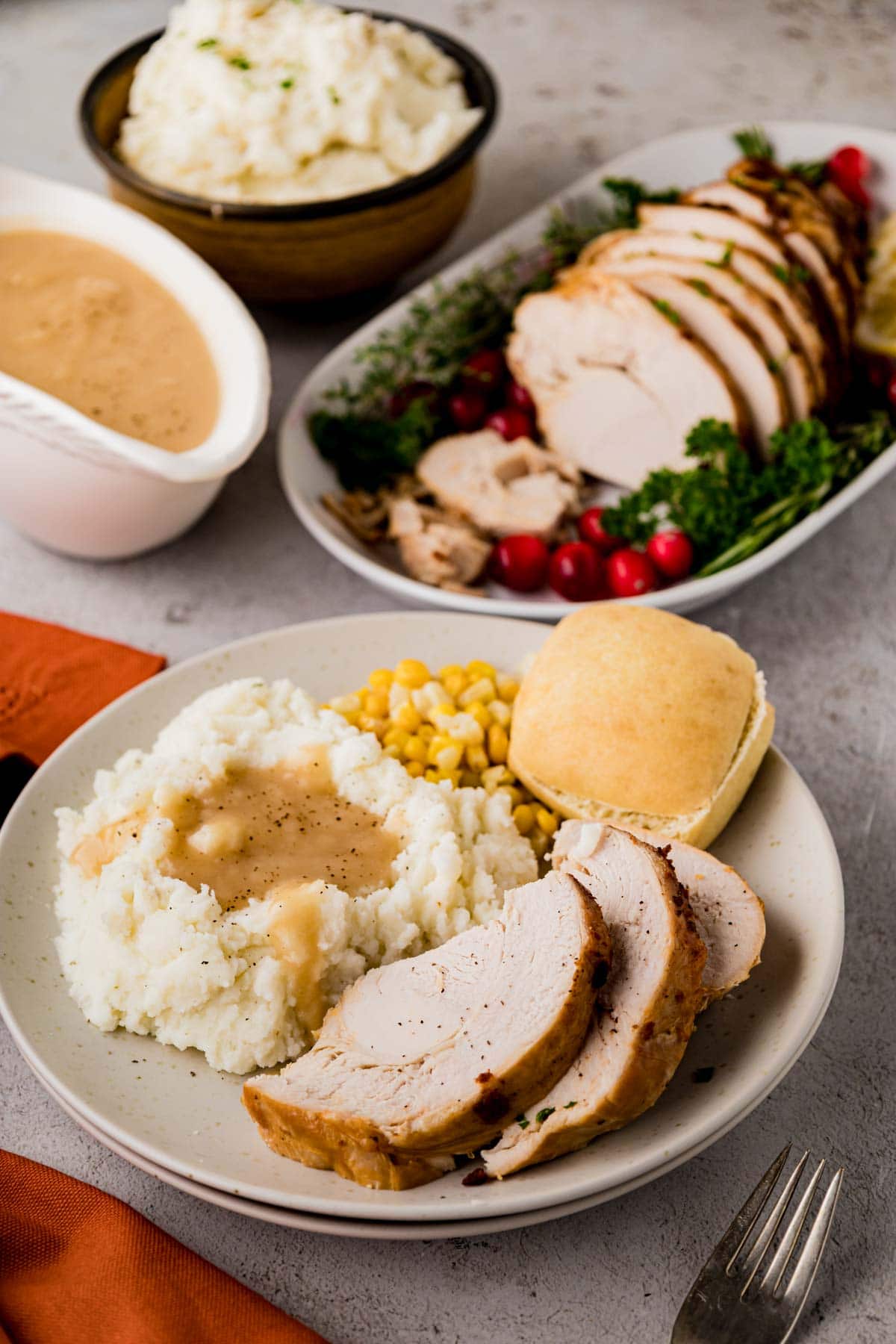 A white plate filled with sliced turkey, mashed potatoes, gravy, corn, and a roll.