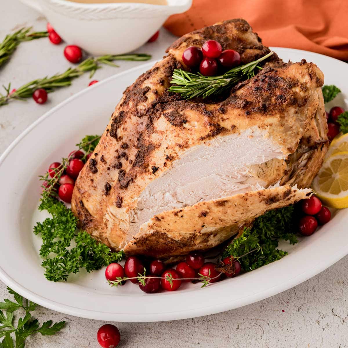 A whole slow cooker, turkey breast on a planter, garnished with lemon slices, parsley rosemary, and cranberries.