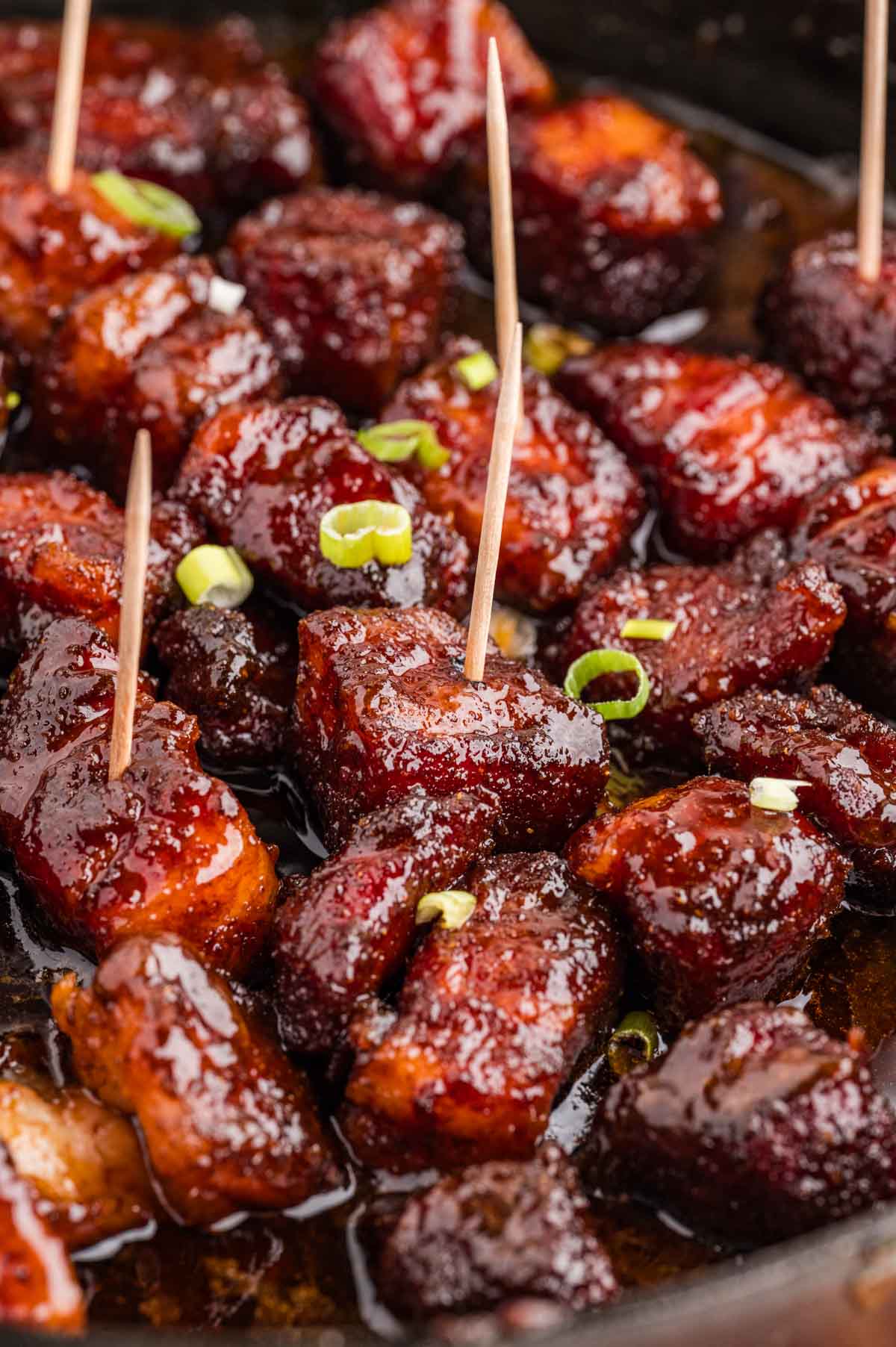 Close up of pork belly burnt ends in a skillet with some toothpicks in a few of them.