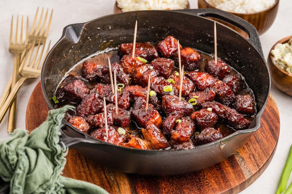 Smoked pork belly burnt ends served in a cast iron skillet with toothpicks for serving.