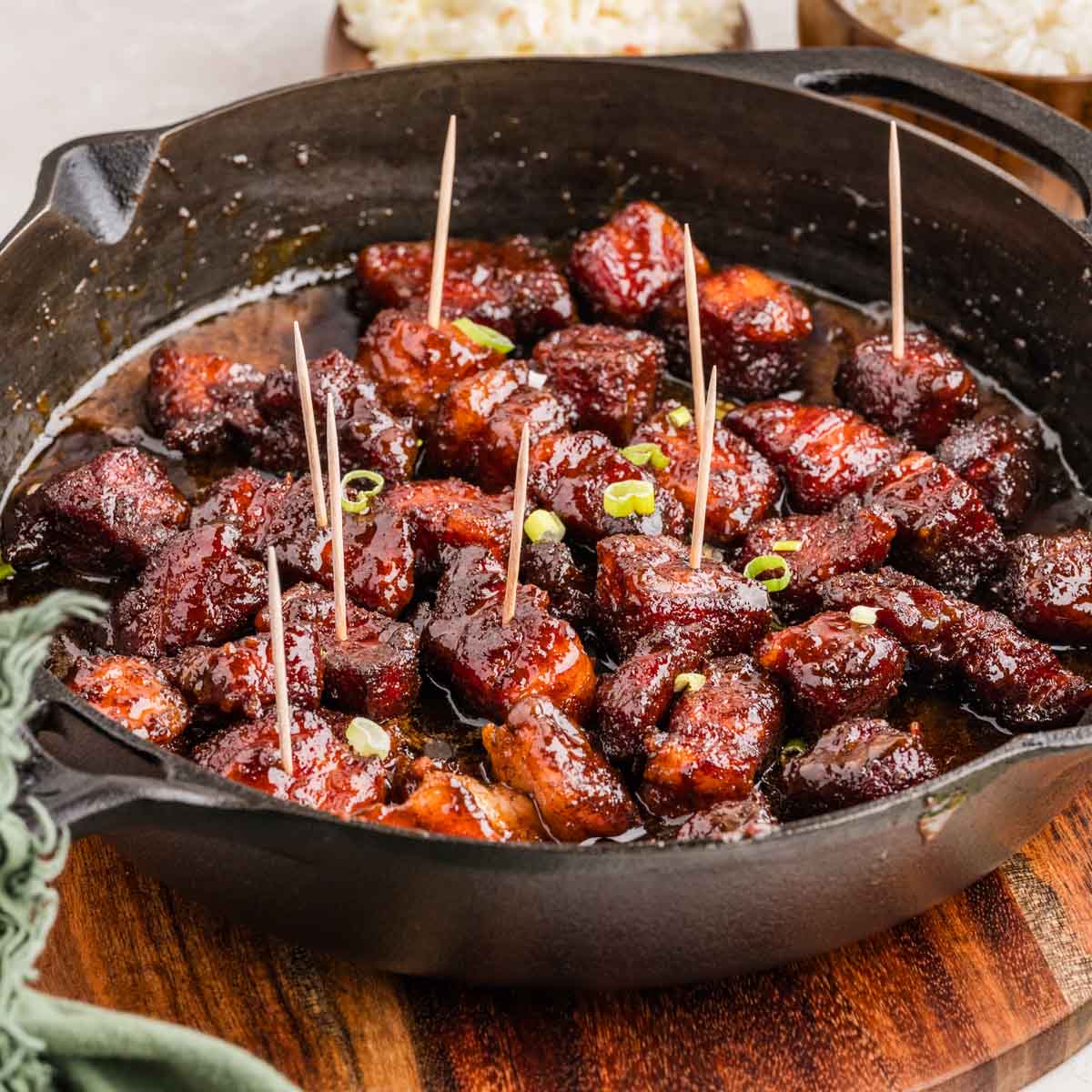 Finished smoked pork belly burnt ends in a cast iron skillet with toothpicks in some of them.