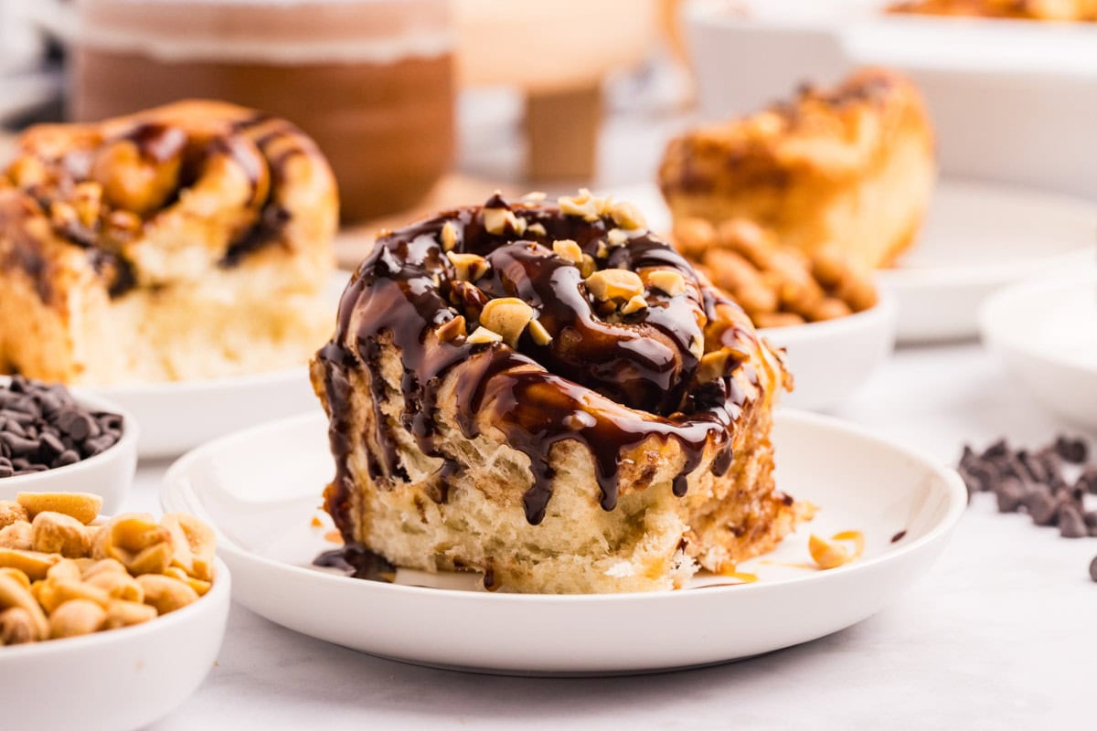 Snickers roll served on a plate with fudge sauce dripping down it.