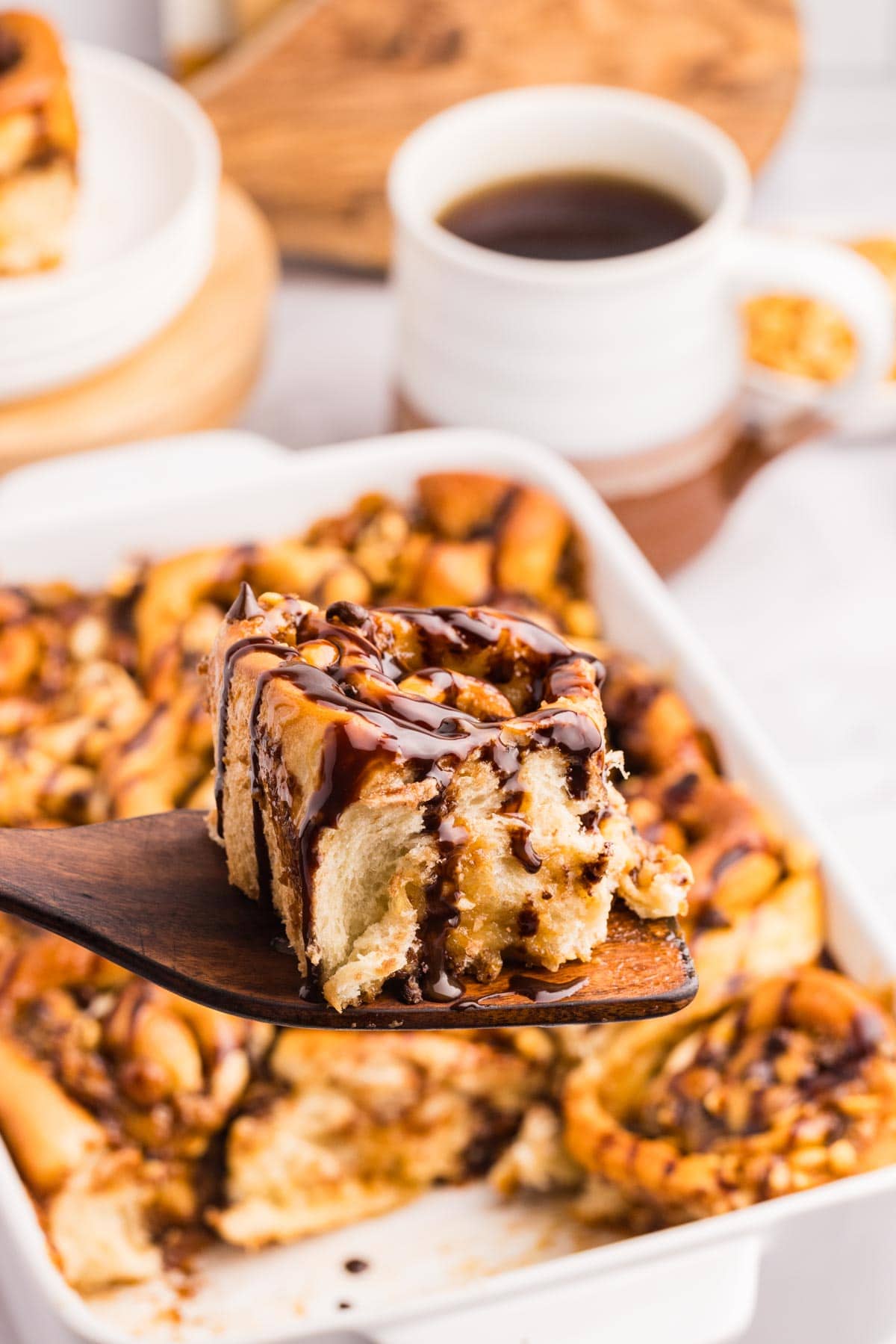 Side view of a snickers roll on a wooden spatula with more snickers rolls in the background.